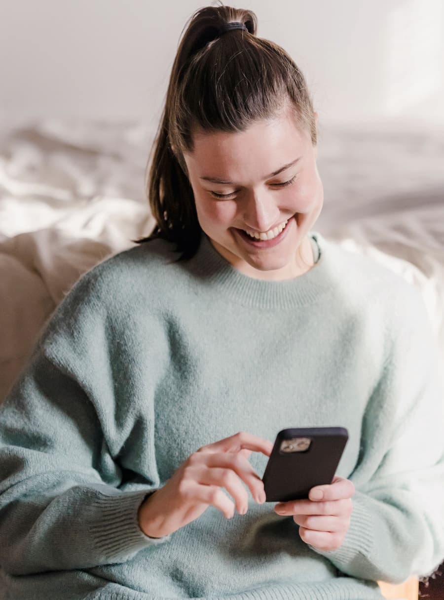 A woman smiling warmly while looking at her phone at home